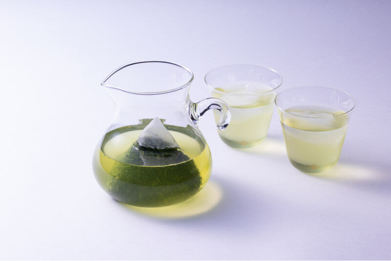 Teapot-sized Shincha Teabag steeping in a glass pitcher of cold brewed light green tea beside two glasses of sencha tea.