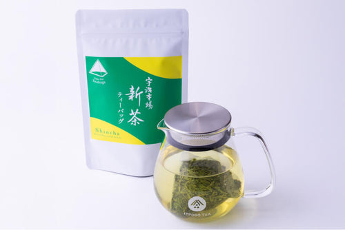 Glass teapot with Shincha Teapot-Size Teabag, brewed light green tea. Package behind with bright green and yellow label.