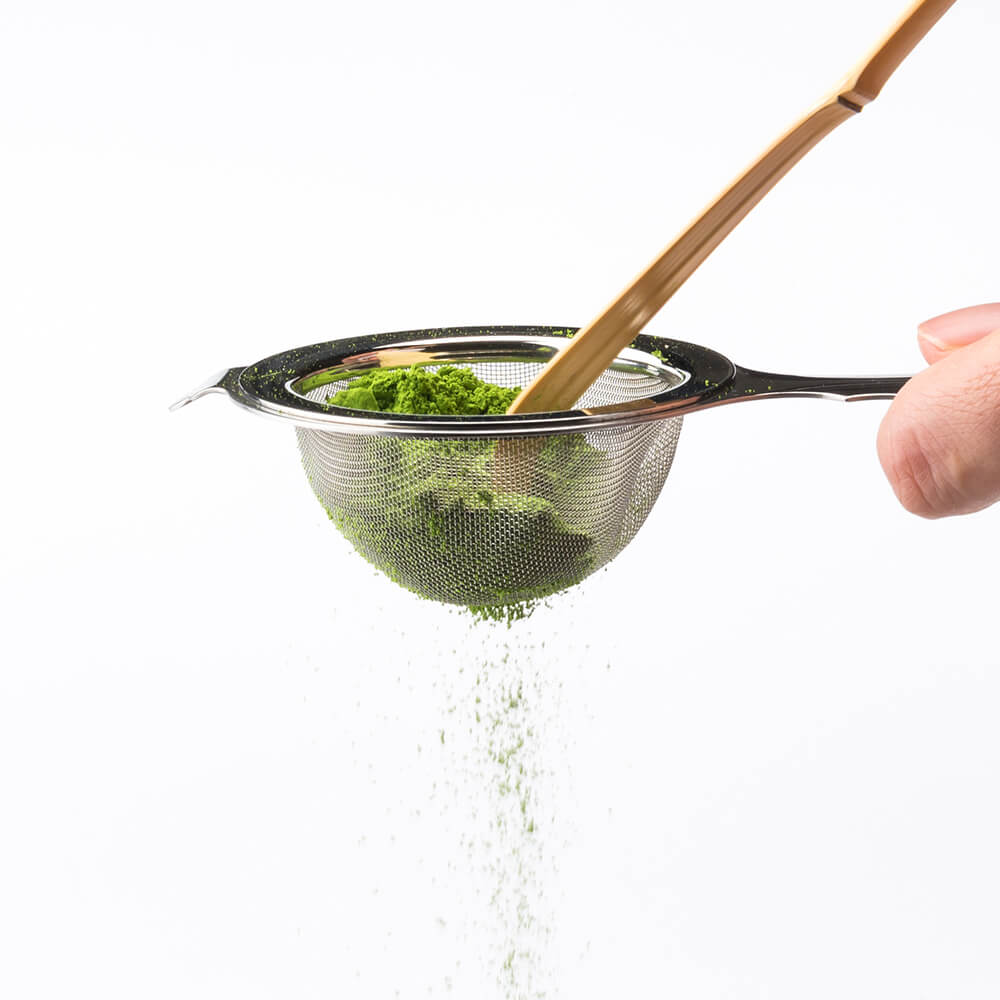 Vibrant green Ippodo matcha powder being sifted through Chakoshi tea strainer with Chashaku bamboo tea ladel 