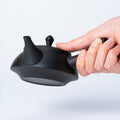 Hand holding black Ippodo Tea kyusu. Traditional Japanese teapot with side handle, ready to pour. 