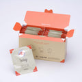 Open box filled with Ippodo hojicha tea bag packets with orange accents, alongside a single hojicha packet in front. - thumbnail 1