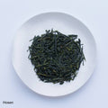White plate of dark green most popular loose leaf Ippodo Tea Hosen Sencha Japanese tea leaves on white table