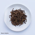Sample of dried brown stems from Ippodo (Kuki) Stems Hojicha roasted bancha green tea stems on white plate, on white table