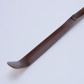Mahogany brown curved matcha tea ladle utensil on a light gray background