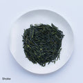 White plate of dark green classic loose leaf Ippodo Tea Shoike Sencha Japanese tea leaves on white table