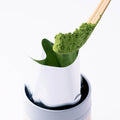 Heaping scoop of green matcha powder on chashaku bamboo tea ladle above opened foil pouch in white Ippodo Tea tin