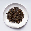White plate of brown loose dried roasted organic Japanese green tea Organic Hojicha by Ippodo Tea Co. on white table