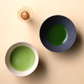 Thin frothy usucha matcha in cream tea bowl and thick koicha matcha in dark tea bowl and chasen bamboo whisk on beige table - thumbnail 3