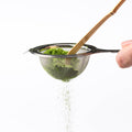 Vibrant green Ippodo matcha powder being sifted through Chakoshi tea strainer with Chashaku bamboo tea ladel