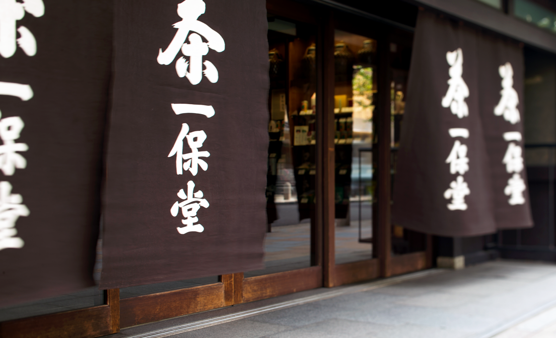 Glass doors at Kyoto storefront between banners labeled Ippodo Tea in Japanese acting privacy blinds shading tearoom inside