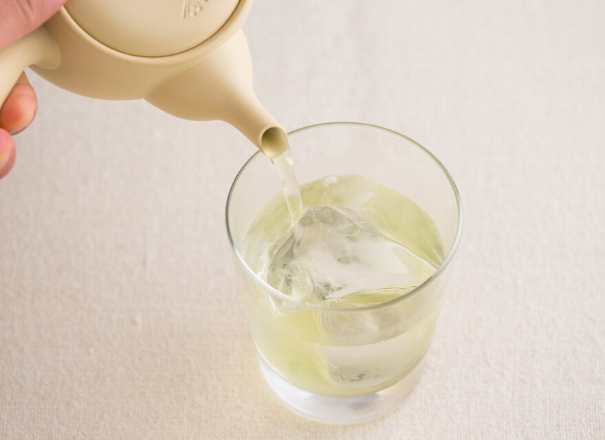 Pouring green tea from ivory Tokoname-yaki ceramic kyusu teapot over ice in small glass