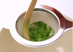 Top view of vibrant green Ippodo matcha powder being sifted through Chakoshi tea strainer with Chashaku bamboo tea ladel