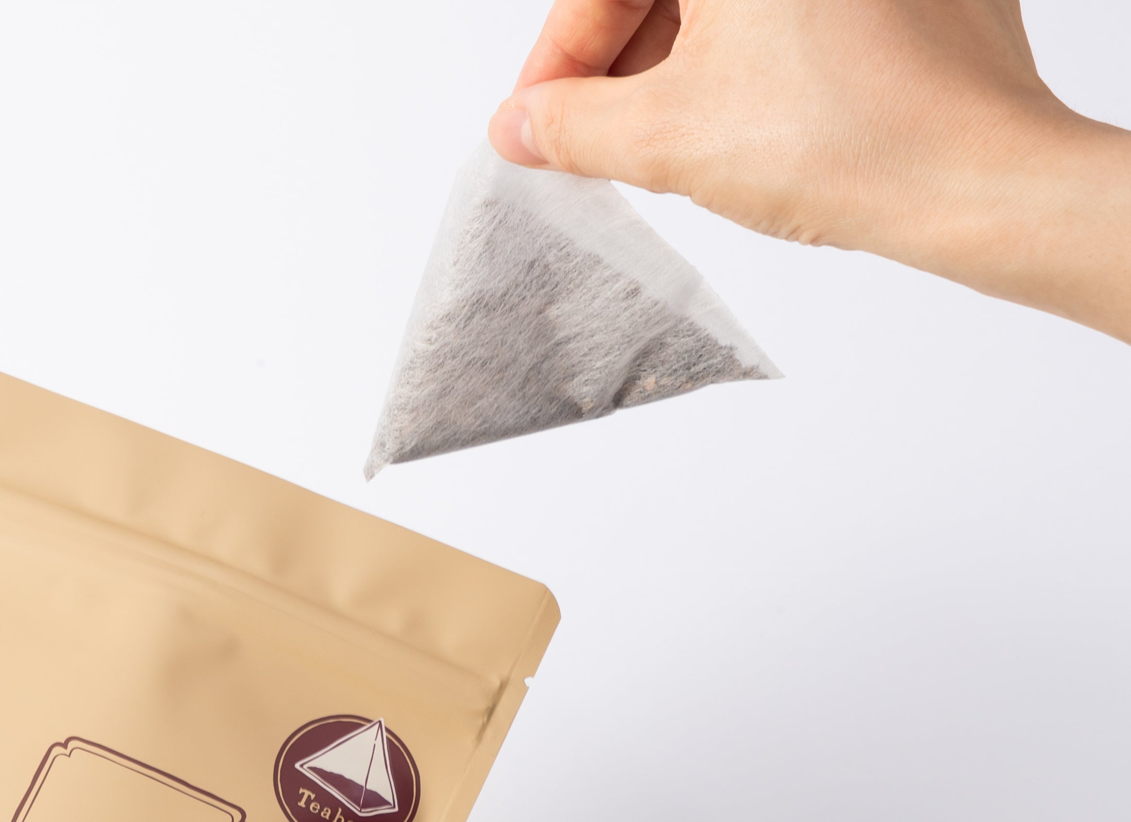 Hand pulling pyramid-shaped Iribancha teabag out of packaging. - Iribancha Teabags - Hot Brew - Kyusu