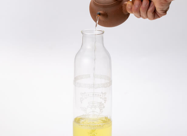 Pouring hot steamy water from stainless steel tea kettle into brown clay side-handle Japanese Yakishime Kyusu on wooden table