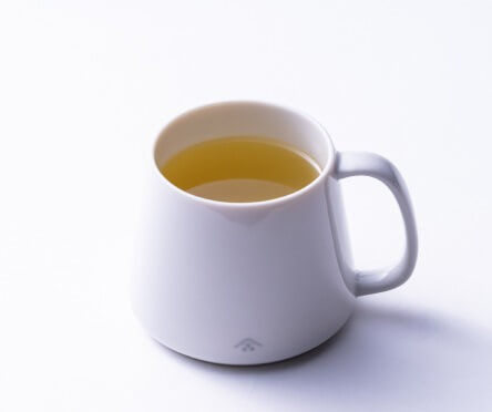 Mug of steeping tea drip teabag clipped onto top beside plate of wagashi dessert