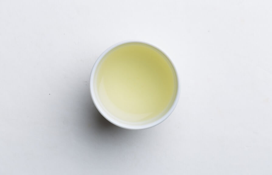 Top-down view of light green brewed Shincha New Harvest Tea by Ippodo in a white Japanese porcelain teacup.