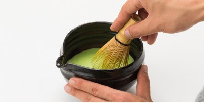Holding black ceramic tea bowl with spout whisking thin usucha Ippodo Tea Ummon matcha with Chasen bamboo 80-tip whisk