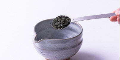 Hand pouring bright green usucha matcha from Black Tea Bowl with Serving Spout into two white Japanese tea cups
