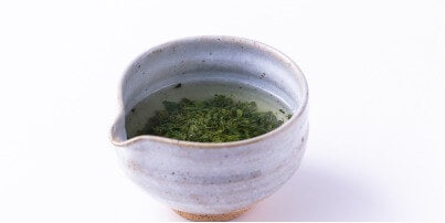 Loose leaf Ippodo green tea brewing in ceramic grey tea bowl with hand groove and serving spout made from Japanese clay